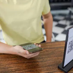 Osoba skanuje telefonem kod QR z menu na stoliku.
