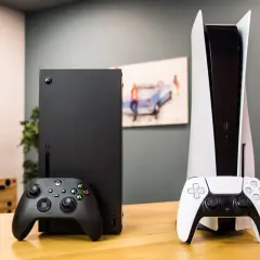 Konsola Xbox Series X i PlayStation 5 z kontrolerami na drewnianym stole.