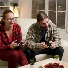 Para grająca w gry wideo na kanapie, trzymająca kontrolery.