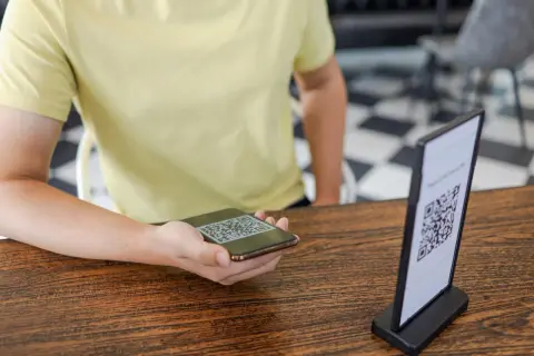 Osoba skanuje telefonem kod QR z menu na stoliku.
