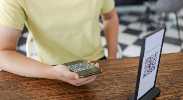 Osoba skanuje telefonem kod QR z menu na stoliku.