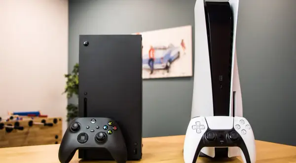 Konsola Xbox Series X i PlayStation 5 z kontrolerami na drewnianym stole.