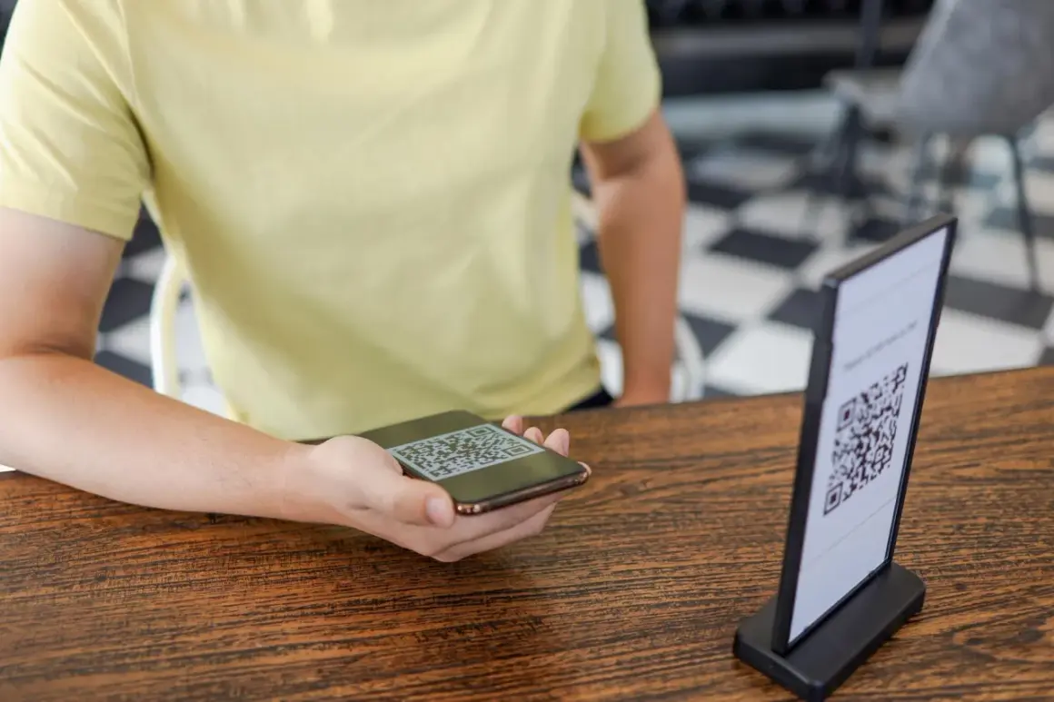 Osoba skanuje telefonem kod QR z menu na stoliku.